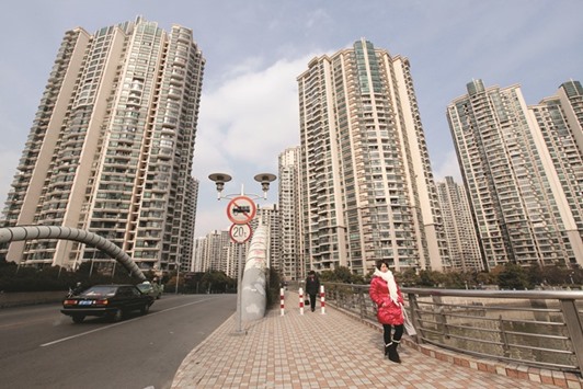 A woman walks in front of a housing complex in Shanghai. Debt rating companies say Chinese builder bonds are at risk of downgrades to junk, after borrowing heavily to buy land as prices surged.