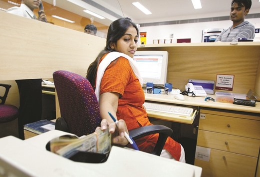 A cashier at the ICICI bank branch in New Delhi places rupee notes in a counting machine. The Indian currency will decline to an unprecedented 69.50 per dollar by the end of the year, 3.5% weaker than its close in Mumbai yesterday, according to Kotak Mahindra Bank.