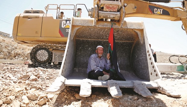 A man holding a Palestinian flag protests as he sits in the scoop of an Israeli excavator as tries to prevent it from clearing his land during a protest against Jewish settlements, near the village of Deir Qaddis near the West Bank city of Ramallah yesterday.