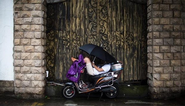 A man uses an umbrella to protect himself against the rain while having a nap on his scooter in Shanghai on Thursday.