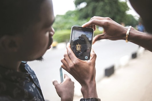 Timi Ajiboye (left) and Tobi Akinnubi try and catch a Pokemon while using the Pokemon Go application on their mobile on the campus grounds of the University of Lagos.