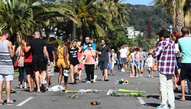 People walk by flowers placed on stains on the pavement at the Promenade des Anglais in Nice as tribute to the victims of the deadly Bastille Day attack, on July 16, 2016
