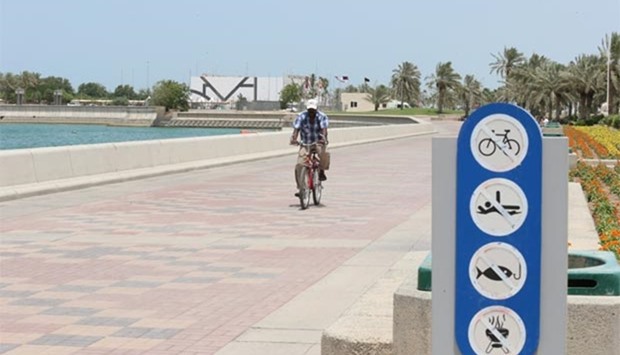 A man rides a bicycle on the Corniche near a signboard that bars cycling.