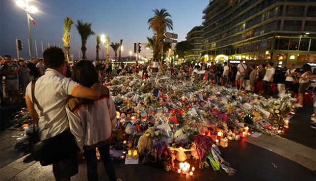People stand in front of flowers, candles and messages laid at a makeshift memorial in Nice on July 18, 2016, in tribute to the victims of the deadly attack on the Promenade des Anglais seafront which killed 84 people.