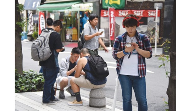People hold their mobile phones while standing in the street playing Nintendou2019s Pokemon Go game at Akihabara shopping district in Tokyo yesterday. The augmented-reality game Pokemon Go, which has been released in more than 40 countries, was finally launched in its native market Japan where Nintendo created the franchise two decades ago.