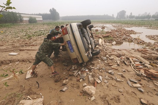 People push a car that turned over during floods in Xingtai, Hebei Province.