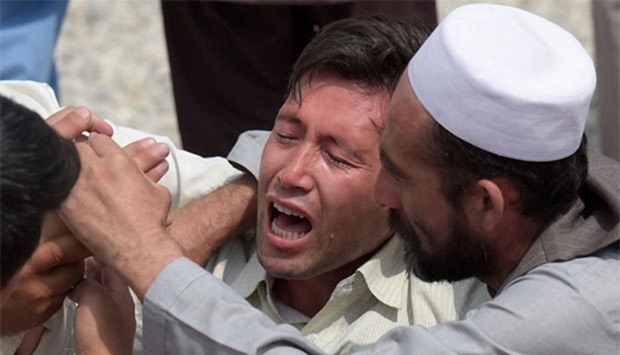 A relative is comforted as he weeps alongside unseen shoes and other belongings of those who were killed in the twin suicide attack, at a mosque in Kabul on Sunday.