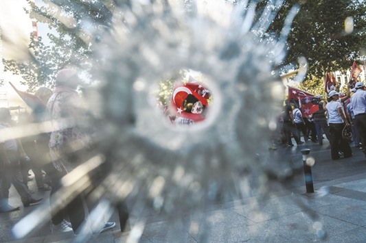 Demonstrators seen through a bullet hole in a hotel window near Istanbulu2019s Taksim Square wave Turkish flags on Sunday during the first cross-party rally to condemn the coup attempt against President Recep Tayyip Erdogan.