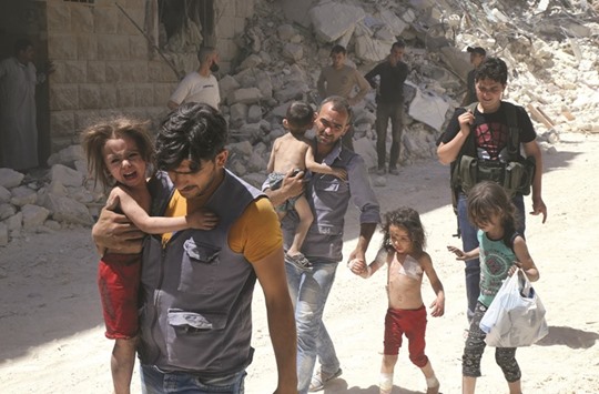 Syrian men carry injured children amid the rubble of destroyed buildings following reported air strikes on the rebel-held neighbourhood of Al-Mashhad in the northern city of Aleppo, yesterday.