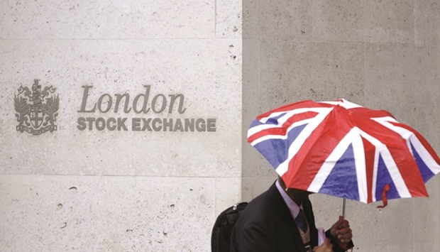 A worker shelters from the rain as he passes the London Stock Exchange. Londonu2019s FTSE 100 slipped 0.3% to 6,710.13 points yesterday, led downwards by oil companies as prices fell.