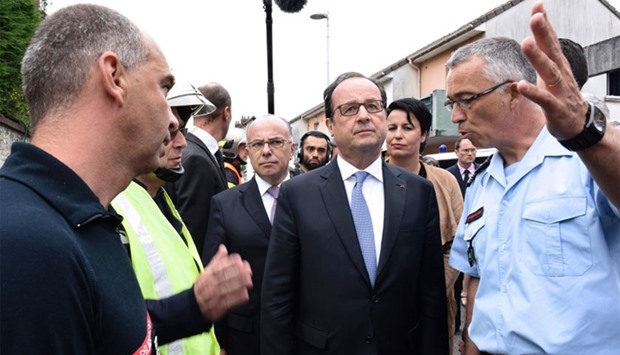 French President Francois Hollande (C), followed by French Interior Minister Bernard Cazeneuve (L), listens to French fireman officer as he arrives in Saint-Etienne-du-Rouvray after a hostage-taking at a church of the town on July 26, 2016 that left the priest dead.