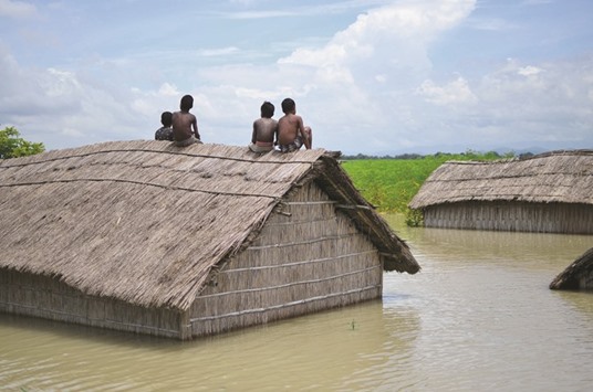 Two children sit on the roof of a home submerged in flood waters in Batahidia in South Kamrup, southwest of Guwahati, in Assam yesterday.
