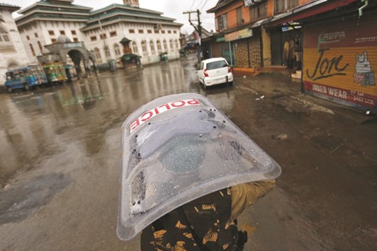 A policeman uses his shield to cover himself from rain as he patrols a deserted road during a curfew in downtown Srinagar yesterday.
