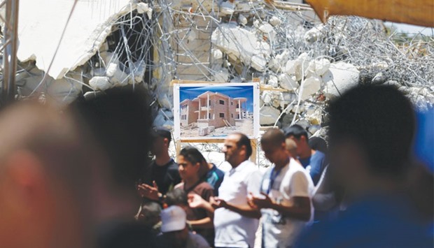 Palestinian worshippers perform the Friday prayer next to the rubble of the Palestinian homes that were destroyed by Israeli authorities three days before, yesterday in the village of Qalandia, which is located next to Israelu2019s controversial separation barrier, between the West Bank town of Ramallah and East Jerusalem. On July 26 Israeli authorities demolished a dozen Palestinian homes in Qalandia, according to Palestinian sources. Witnesses added that shortly after midnight, a convoy of dozens of military vehicles and Israeli bulldozers stormed the area, before demolishing 11 houses. Israeli authorities did not respond to requests for information on the demolitions, but such cases are usually said to be because the owners did not have building permits.