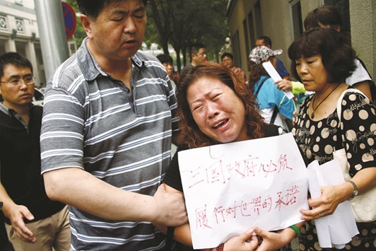 A family member of a passenger aboard flight MH70 breaks down during a protest outside the Chinese foreign ministry in Beijing yesterday. The placard reads: u2018The three governments have an obligation to the world to carry out their promise.u2019