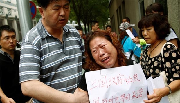 A family member of a passenger aboard Malaysia Airlines flight MH370, which went missing in 2014, reacts during a protest outside the Chinese foreign ministry in Beijing on Friday. The placard reads ,The three governments have an obligation to the world to carry out their promise.,