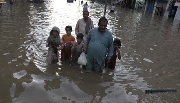 A Pakistani family wade through a flooded street following a heavy rain in Lahore, Pakistan