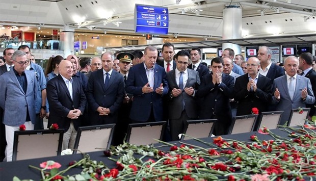 Turkish President Recep Tayyip Erdogan (C) praying near flowers and portraits of the victims of the Istanbul Ataturk Airport attack at the International departure terminal in Istanbul on July 2, 2016