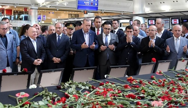 Turkish President Recep Tayyip Erdogan (C) praying near flowers and portraits of the victims of the Istanbul Ataturk Airport attack