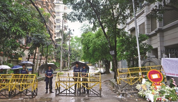 Policemen standing under umbrellas at a checkpoint in Dhaka yesterday, in a street leading to the entrance of a restaurant which was the site of a bloody siege that ended in the death of 17 foreigners and five Bangladeshis.