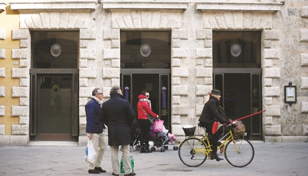 Pedestrians pass a Banca Monte dei Paschi bank branch in Siena. Monte Paschi, saddled with u20ac47bn ($52bn) of non-performing loans, is among the most exposed on a list of weak banks whose pile of bad debts and capital shortfalls are threatening contagion to other European Union nations.