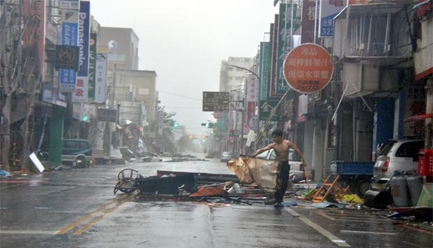 A man is holding onto debris in front of a row of shop fronts damaged by strong winds in Taitung on Friday.