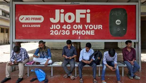 Commuters use their mobile phones as they wait at a bus stop with an advertisement of Reliance Industries' Jio telecoms unit, in Mumbai on Monday.