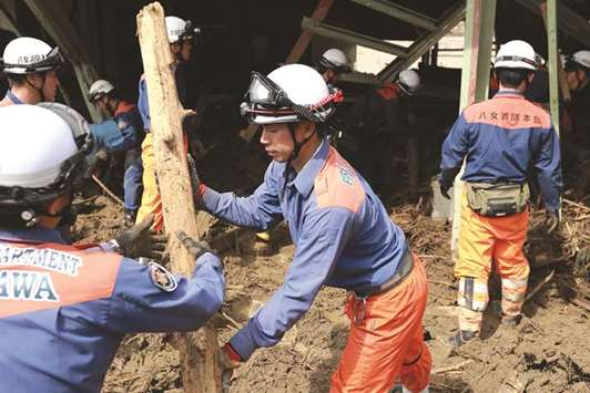 Fire department officers remove debris from a damaged house in a flooded area in Asakura.