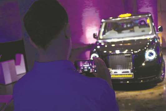 An attendee uses a smartphone to film the new TX electric black taxi, manufactured by the London EV Co, during its unveiling in London on Tuesday. Amsterdamu2019s Rotterdam Mobility Center agreed a 225-vehicle deal for the new all-electric hackney cab that will meet new pollution rules in the Dutch capital. It will be delivered from a factory near Coventry, England, in the first quarter of 2018, the companies said.