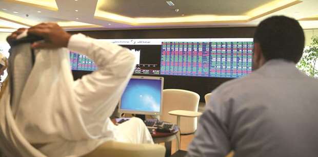 Traders sit behind their desks in front of the Qatar Stock Exchange board in Doha (file). The 20-stock Qatar Index yesterday surged 2.04% to close at 9,469.93 points.