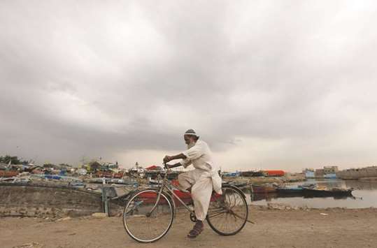 An elderly man rides a bicycle past fishing boats with monsoon clouds behind him, in Karachi, yesterday.