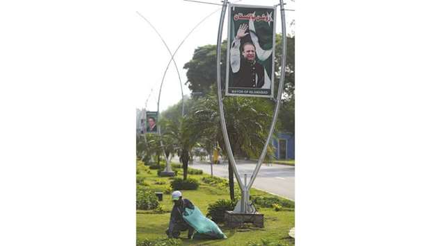 A Pakistani worker cleans a garden under a billboard with the portrait of Pakistani Prime Minister Nawaz Sharif along a street in Islamabad yesterday. The chairman of Pakistanu2019s financial regulator was arrested yesterday, accused of forging documents in a corruption case against Prime Minister Nawaz Sharif that has gripped the country.