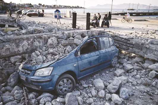 People look at a car crushed under rubble near the port of the Greek island of Kos following a 6.7 magnitude earthquake which struck the region yesterday.
