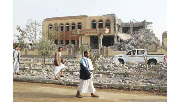 Yemenis walk past a building, housing branches of the Finance Ministry and Central Bank, that was heavily damaged in an air strike by the coalition, in the northern province of Saada yesterday.