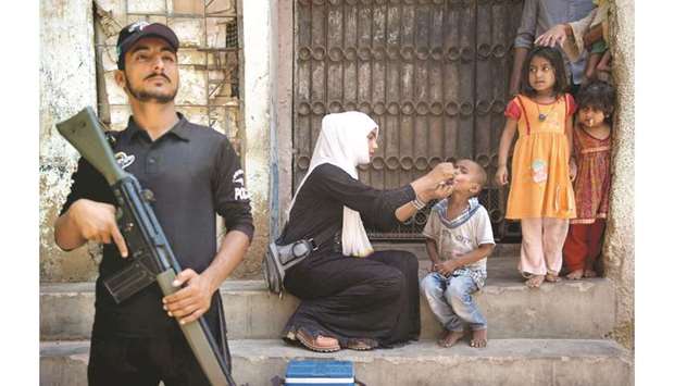 A Pakistani policeman stands guard as a health worker administers the polio vaccine to a child during a vaccination campaign in Karachi.