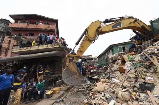 Locals look on as a rescue worker operates a bulldozer in search for bodies in the rubble of a collapsed building in Lagos.