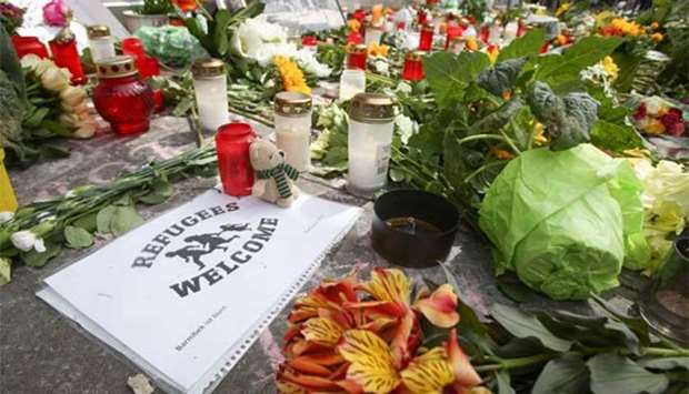 A sign reading ,Refugees Welcome, is placed among flowers and candles at a makeshift memorial for the victims of a knife attack in front of a supermarket in Hamburg.