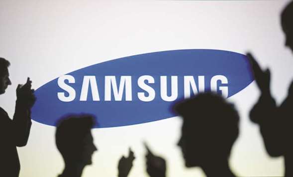 People are silhouetted as they pose with mobile phones in front of a screen projected with a Samsung logo. The company invests more than $10bn in chips annually, helping it stay ahead of competitors such as cross-town rival SK Hynix and Japanu2019s Toshiba.