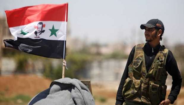 A Syrian army soldier stands next to a Syrian flag in Umm al-Mayazen, in the countryside of Deraa, Syria, yesterday.