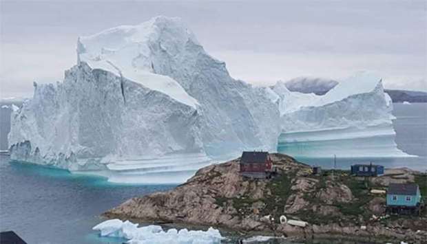 A giant iceberg is seen behind an Innaarsuit settlement in Greenland.