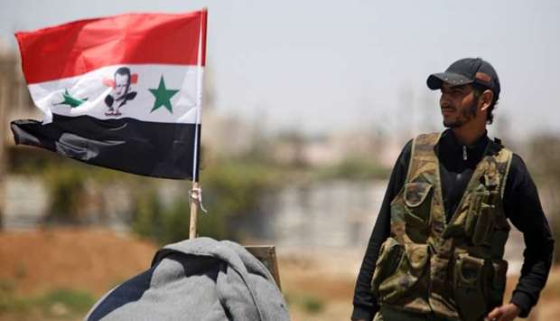 A Syrian army soldier stands next to a Syrian flag in Umm al-Mayazen, in the countryside of Deraa, Syria.
