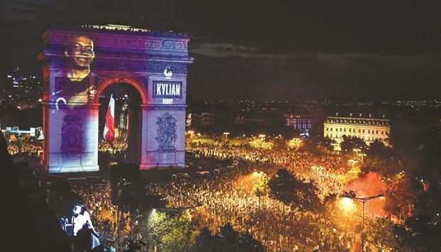 This picture taken from the terrace of the Publicis drugstore shows a portrait of French forward Kylian Mbappe projected on Parisu2019 landmark Arc de Triomphe as people gather to celebrate Franceu2019s victory over Croatia in the final of the World Cup.