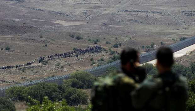 Israeli soldiers look on towards people standing next to the border fence between Israel and Syria from its Syrian side as it is seen from the Israeli-occupied Golan Heights near the Israeli Syrian border.