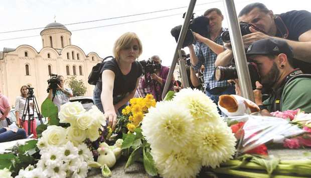 Photographers take pictures as a woman lays flowers at a temporary memorial in front of the Dutch embassy in Kyiv.
