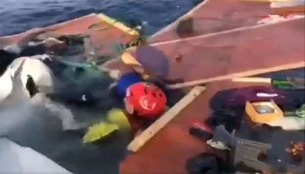 A member of the rescue team (wearing red helmet) of  Proactiva Open Arms searches the wreckage of a migrant boat for survivors