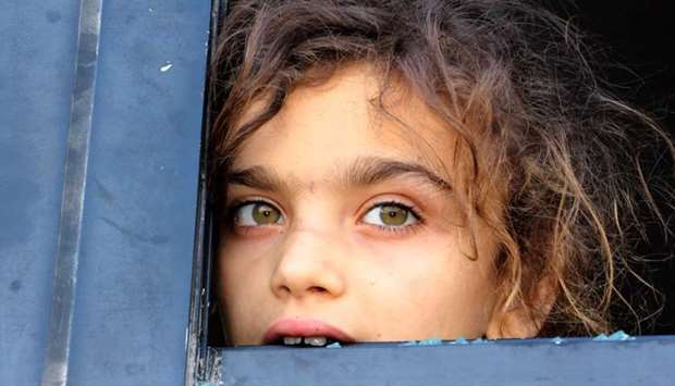 An evacuated Syrian girl from the area of Fuaa and Kafraya in the Idlib province, looks out of a broken bus window as it passes the al-Eis crossing south of Aleppo during the evacuation of several thousand residents from the two pro-regime towns in northern Syria