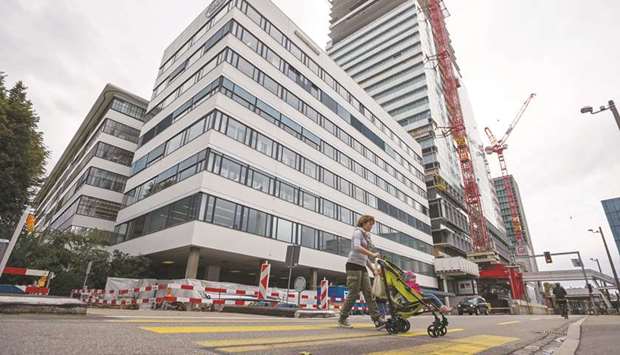 A pedestrian pushes a baby stroller as she crosses an intersection outside Roche Holding headquarters in Basel, Switzerland (file). Roche, Bayer and Merck KGaA became the latest companies to freeze prices in the United States following criticism by the Trump administration of the cost of medicine.