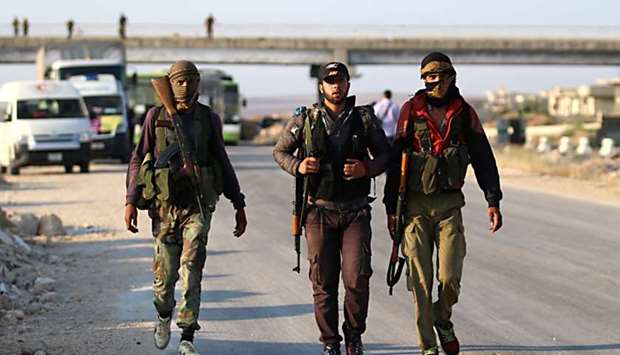 Syrian rebel fighters from the Quneitra province walk with their rifles as they wait at the Murak crossing point to be carried in the provinces of Idlib and Aleppo, in Murak.
