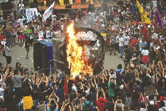Anti-government protesters burn an effigy of President Rodrigo Duterte, connected to a mock train, a reference to his tax reform law, during a protest in Manila yesterday.