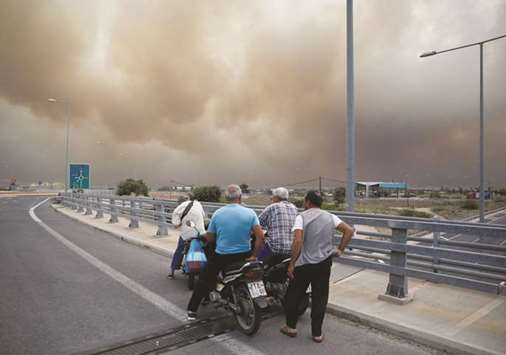 People are seen watching smoke from a wildfire in Kineta, near Athens.